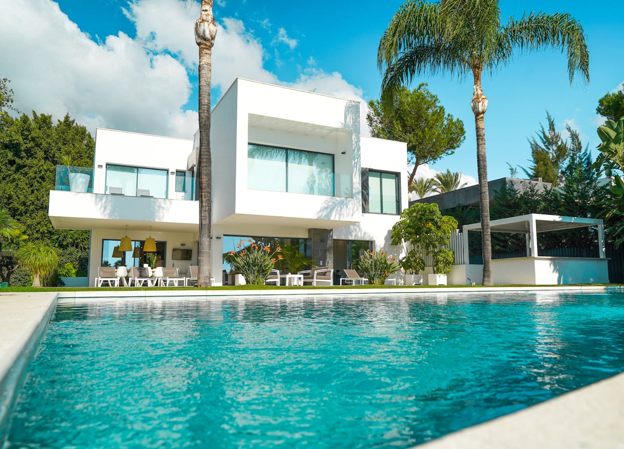 A stunning modern luxury villa with a pool, surrounded by lush greenery and bathed in sunlight.